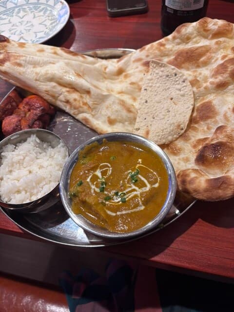 Large nan with curry, tandoori chicken, papad and rice on a thali