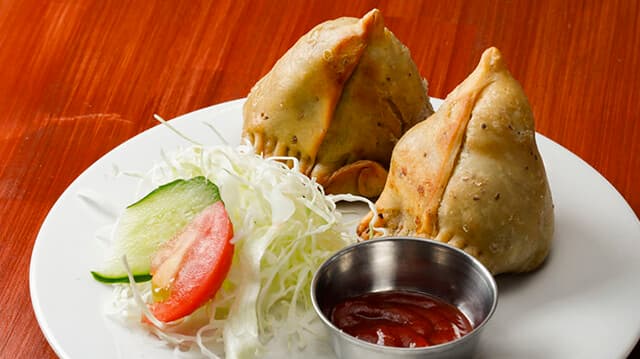 Two golden samosas with shredded cabbage salad and ketchup